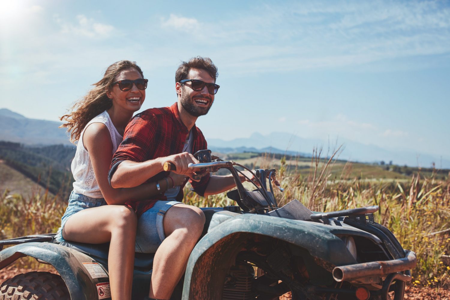 Portrait of loving young couple cruising over country roads by quad vehicle. Happy man and woman driving a quad bike.